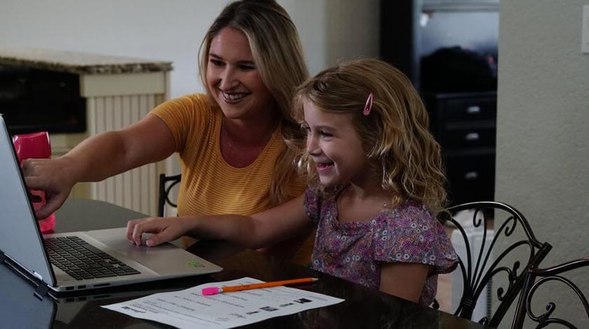 A mother and her dauther are pointing at a computer screen during an online lesson